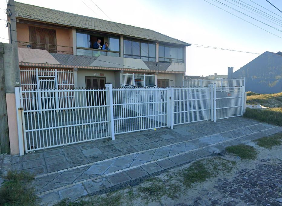 Fachada da pousada vista da calçada, com portão branco e sacada no andar de cima